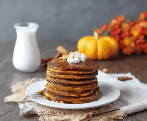 Delicious stack of fluffy coconut flour pumpkin pancakes topped with syrup and fresh berries on a white plate