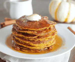 Golden brown sourdough pumpkin pancakes topped with whipped cream and cinnamon, served with fresh pumpkin slices on a rustic plate