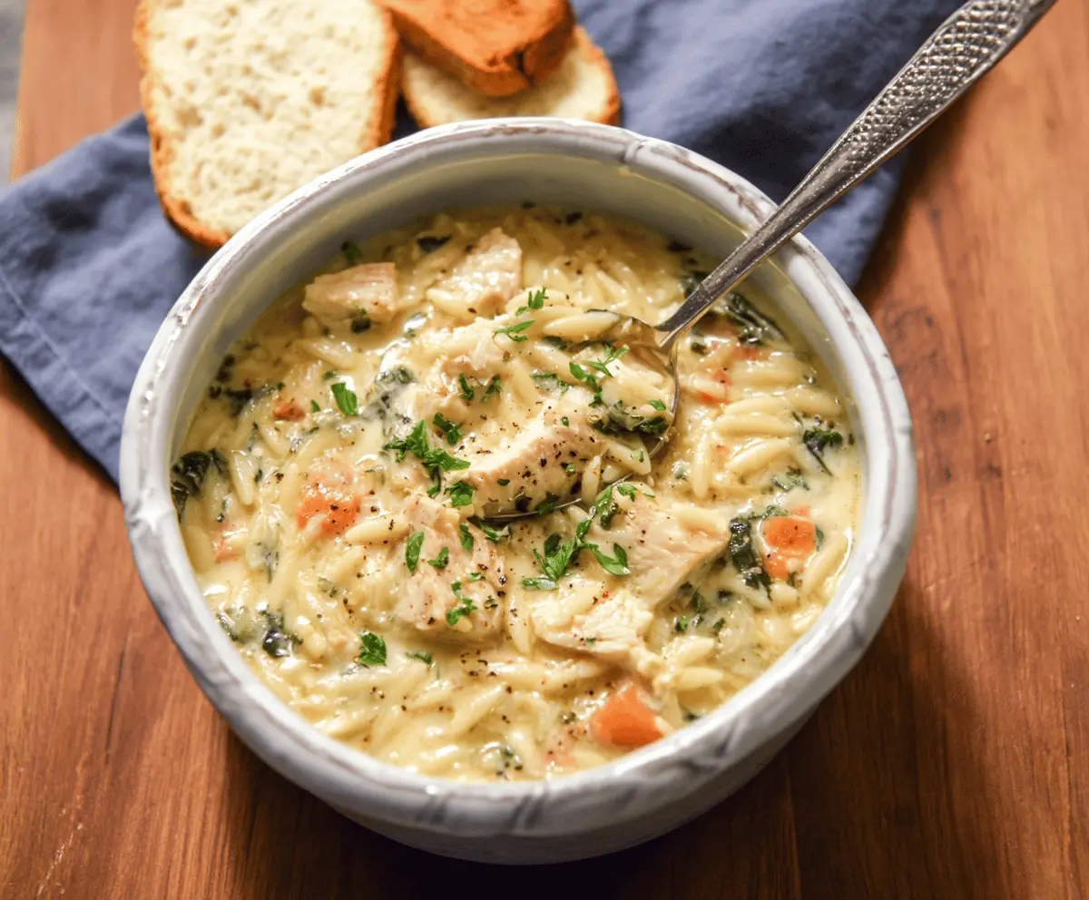 A bowl of creamy chicken orzo soup garnished with fresh herbs, featuring tender chicken, orzo pasta, and a rich, smooth broth.