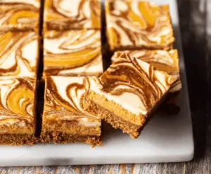 Delicious Pumpkin Swirl Cheesecake Bars topped with whipped cream and cinnamon on a rustic wooden platter, perfect for fall desserts.