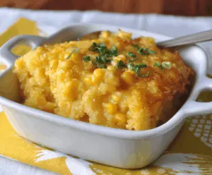 Creamy sweet corn casserole topped with golden brown cheese and fresh herbs, ready to serve as a delicious side dish.