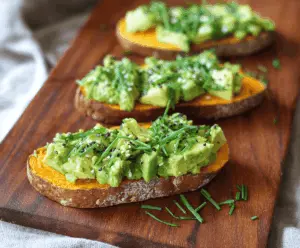 Creamy mashed sweet potatoes topped with ripe avocado slices on whole-grain toast, garnished with herbs for a healthy, flavorful breakfast or snack.