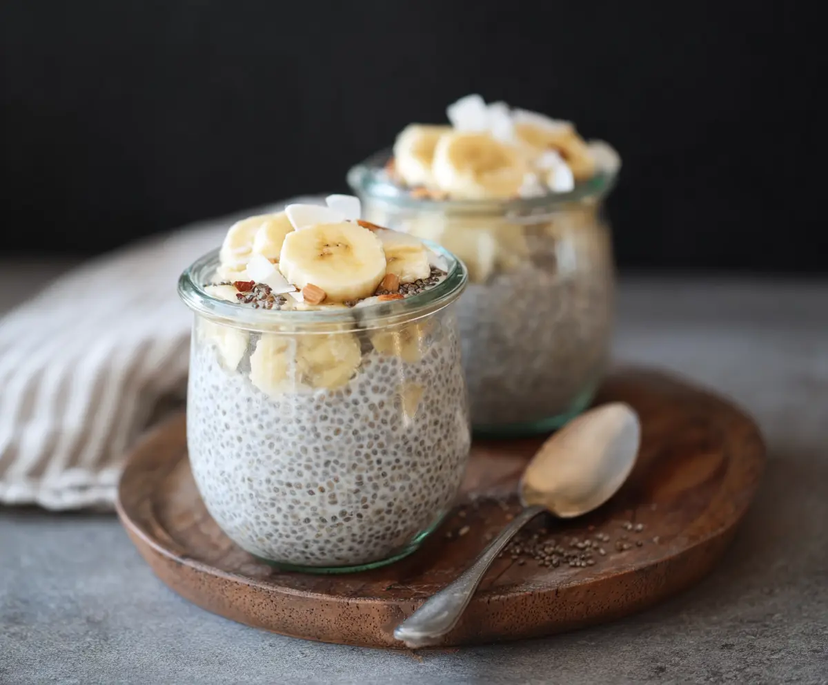 Creamy banana coconut milk chia seed pudding in a glass bowl garnished with fresh bananas and coconut flakes.