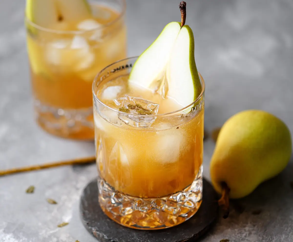 Ginger Pear Bourbon Cocktail in a glass garnished with ginger and pear slices on a bar table.