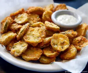 Crispy fried pickles with a golden-brown coating served on a white plate.