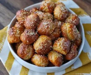 Golden garlic Parmesan pretzel bites served with dipping sauce on a wooden board.