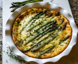 Delicious crustless asparagus quiche served on a white plate, garnished with fresh herbs.