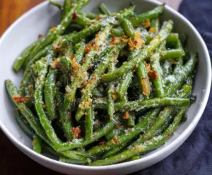 Delicious garlic Parmesan green beans garnished with fresh herbs on a white plate.