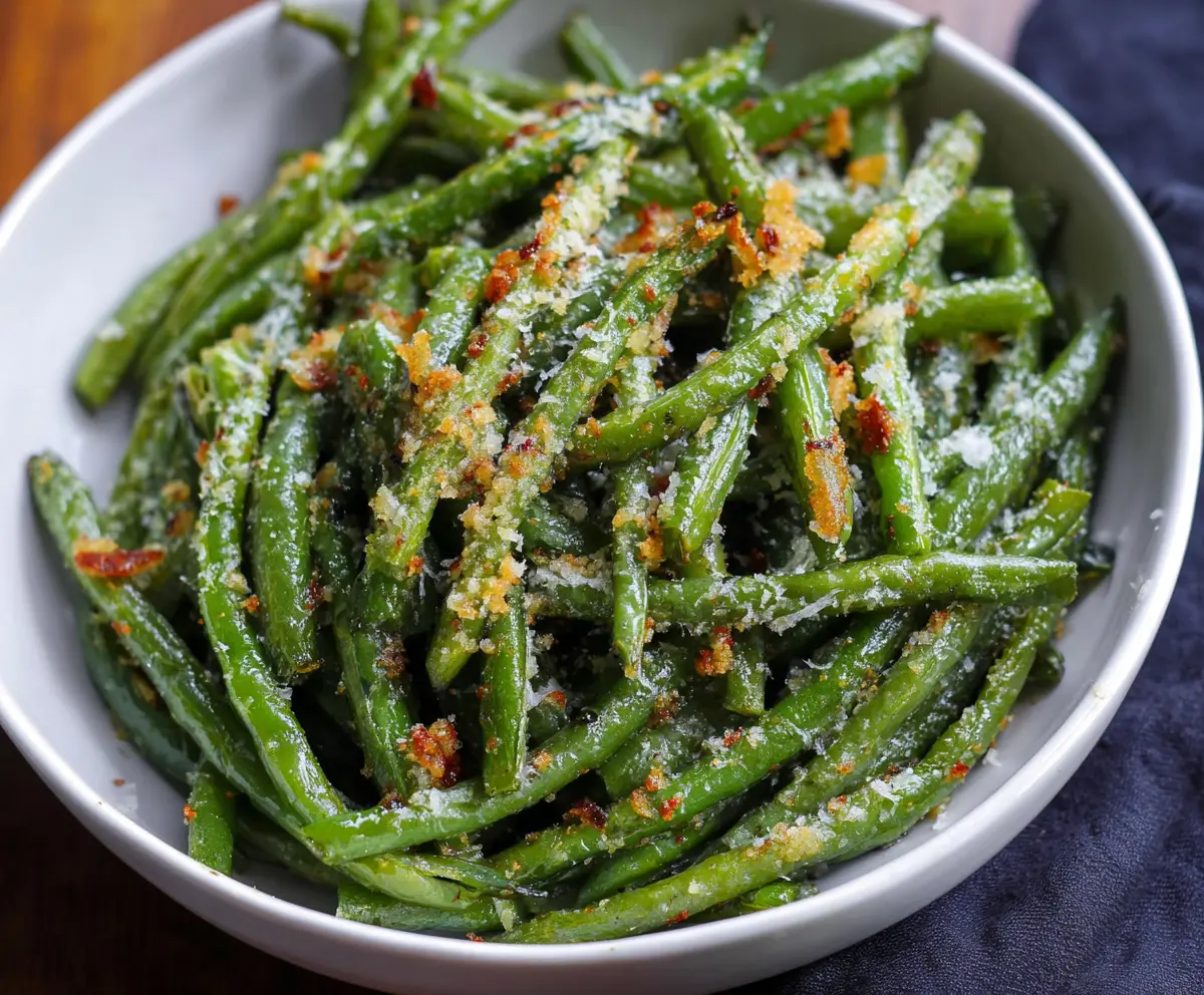 Delicious garlic Parmesan green beans garnished with fresh herbs on a white plate.