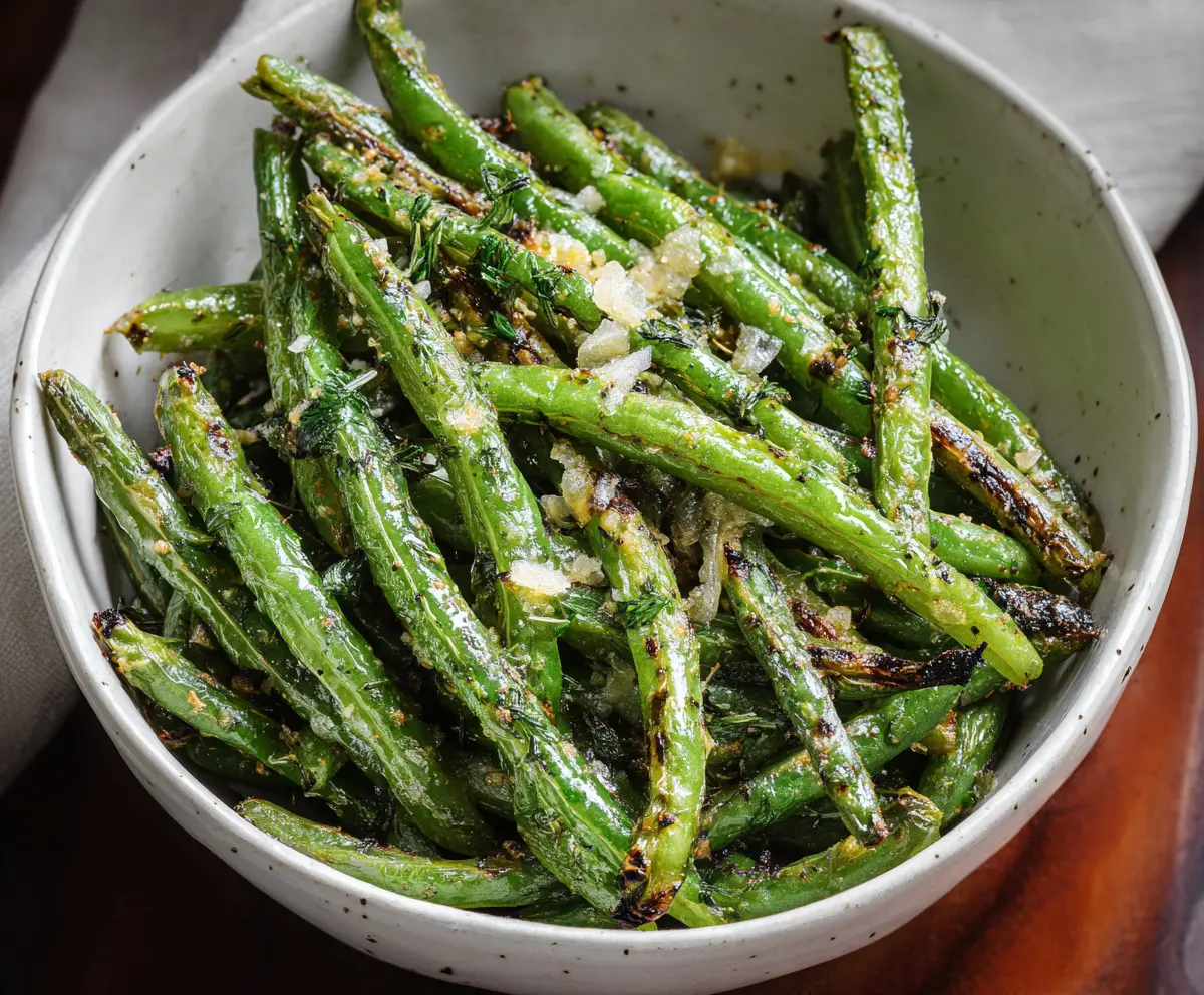 Delicious roasted green beans garnished with herbs on a white plate, perfect as a healthy side dish.
